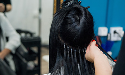 a woman receiving hair extensions treatment in a salon with long black hair and stylists hands applying the extensions for a glamorous look